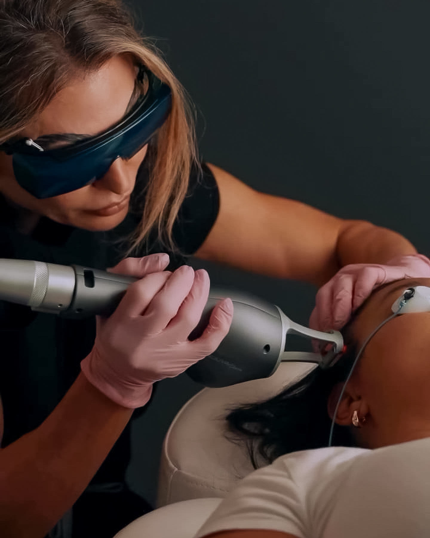 A healthcare professional wearing protective eyewear and pink gloves performs a PlaDuopro treatment on a patient's skin.